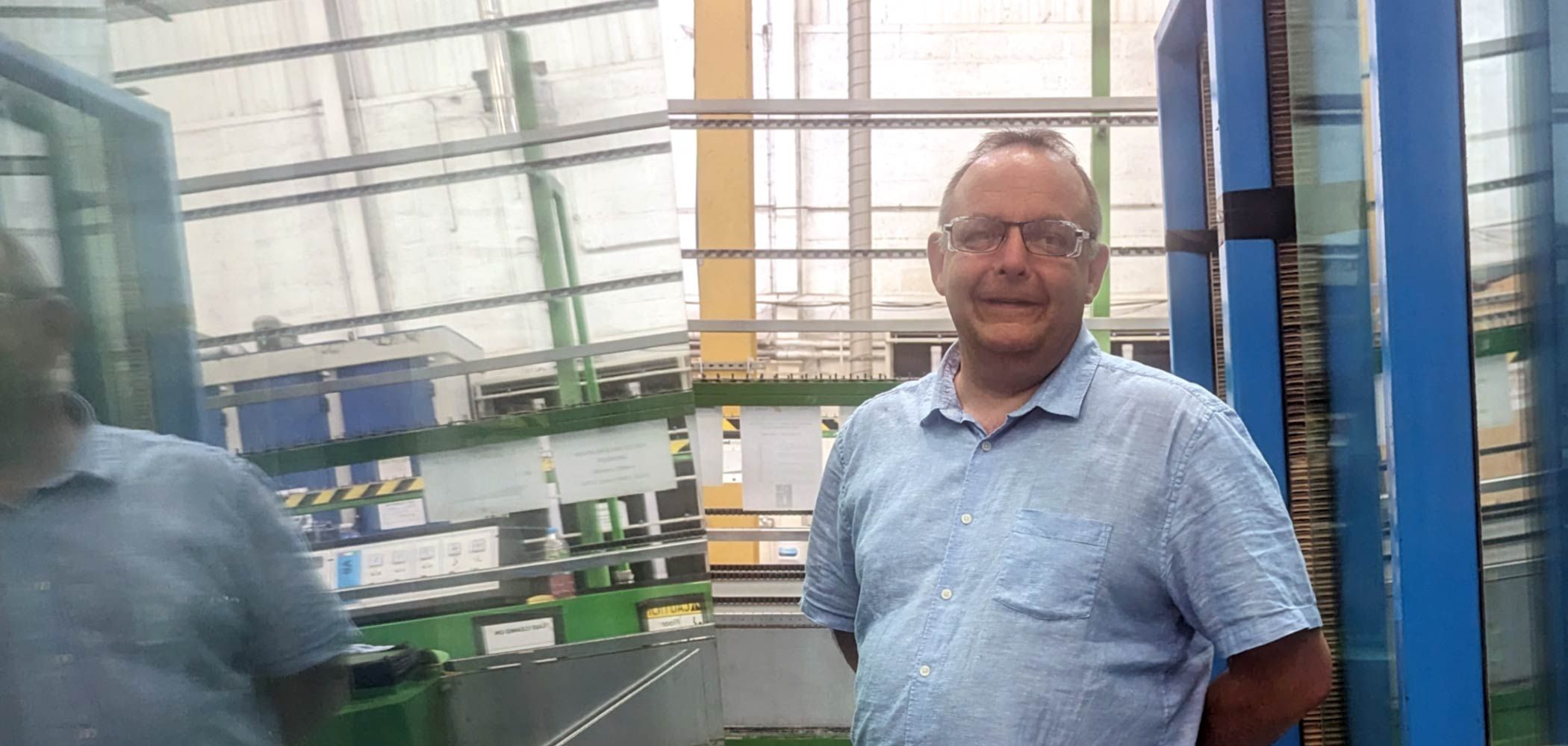 Steve Bunney of Cornwall Glass standing next to glass panes in the workshop